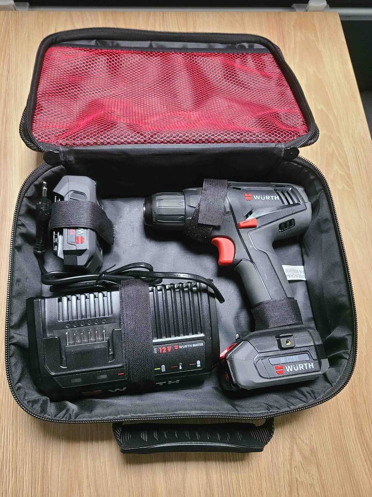 Eine Aufbewahrungstragetasche inklusive Ladegerät, Batterie und des getesteten 12V-Akkuschraubers der Marke Würth, liegt aufgeklappt auf einer Holzoberfläche.