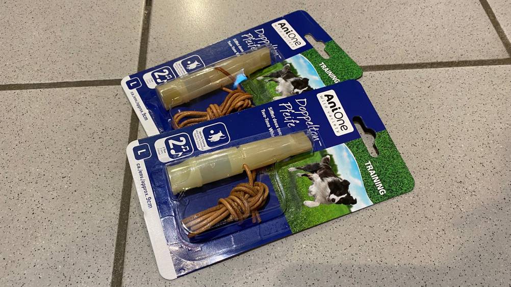 Auf einem Fliesenboden liegen zwei Originalverpackungen von getesteten Hundepfeifen.