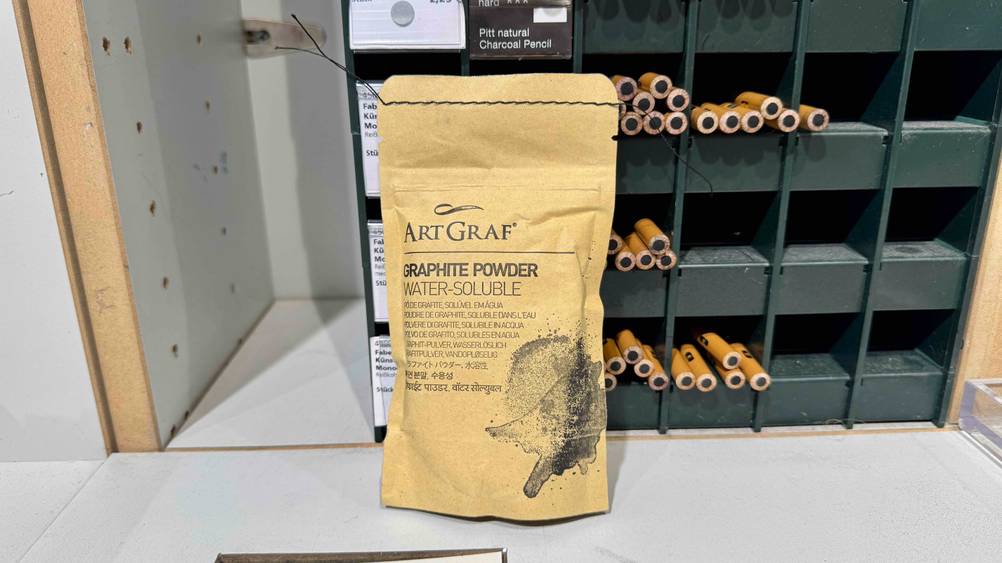 Das getestete Graphitpulver lehnt an einem kleinen Regal worin sich Stifte befinden.