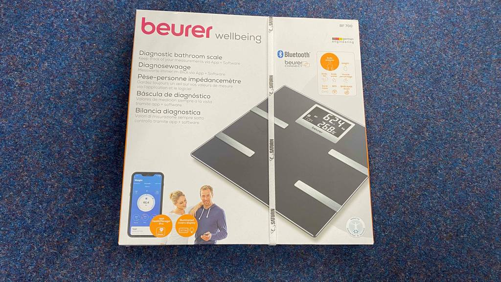 Eine getestete Körperfettwaage mit App originalverpackt auf einem blauen Teppich.
