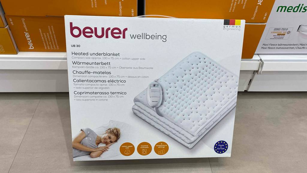 Im Test: Ein verpacktes Wärmeunterbett lehnt an einem Regal mit Produkten.