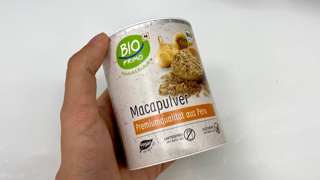 Maca-Pulver getestet: Eine Hand hält eine Packung vor einen hellen Hintergrund