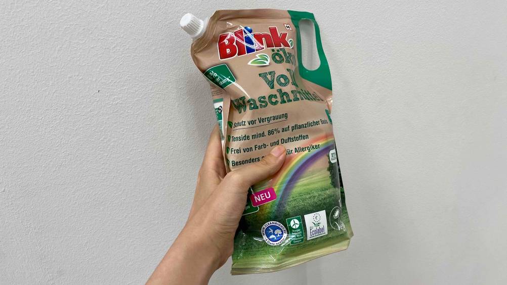 Öko-Waschmittel im Test: Eine Hand hält eine Packung vor eine weiße Wand