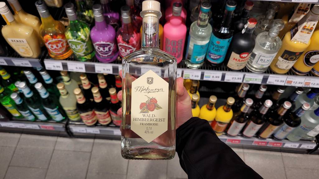 Eine Hand hält eine transparente Flasche mit Himbeerlikör im Test vor ein Regal mit Spirituosen.