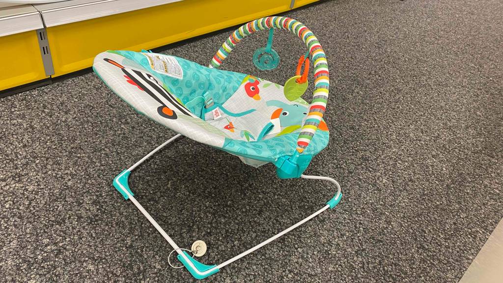 Babywippe getestet: Eine Wippe von schräg hinten vor einem gelben Sockel auf einem grauen Boden.