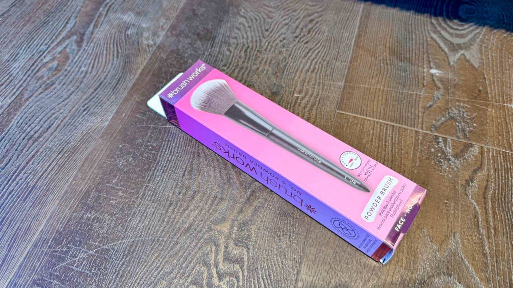 Die Verpackung des getesteten Puderpinsels liegt auf einem Holzboden.