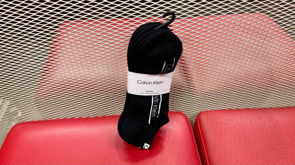 Test: Herrensocken in Schwarz sind in einem 3er-Pack mittels eines Etiketts zusammen gefasst und hängen auf einem Gitter mittels des befestigten Hakens.