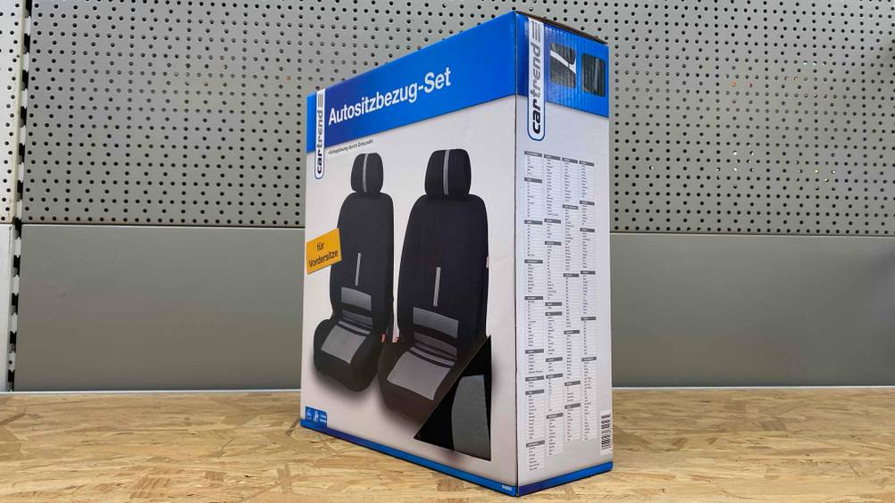 Eine Packung der getesteten Autositzbezüge steht vor einer grauen Wand auf einer Holzfläche.