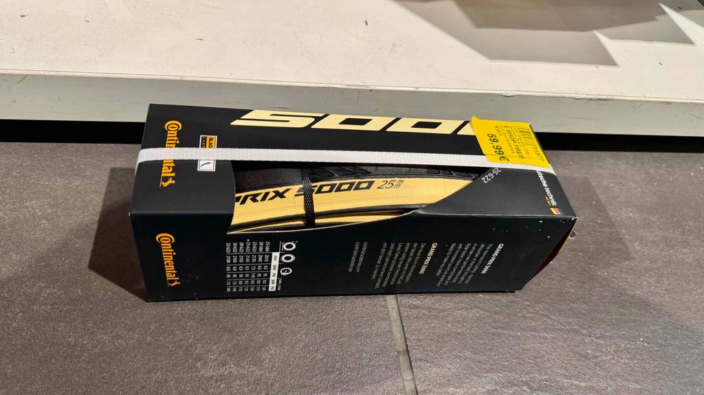 Eine Verpackung des Rennrad-Reifens (25-622) im Test liegt vor einem weißen Regal auf dem Boden.