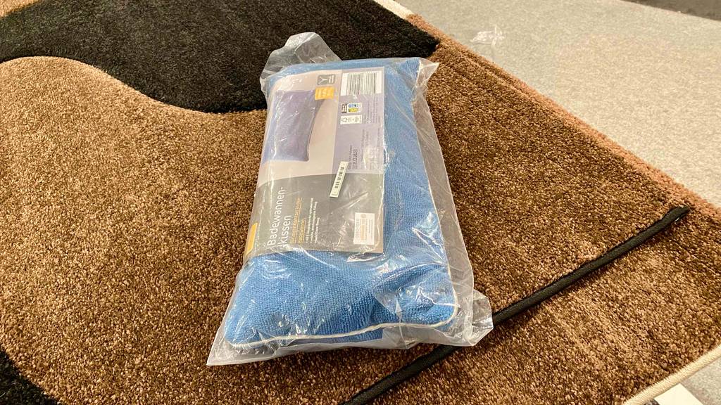 Badewannenkissen getestet: ein eingepacktes blaues Badewannenkissen liegend auf einem Badvorleger.