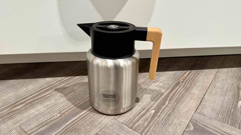 Die getestete Edelstahl-Teekanne mit einem Holzgriff steht auf einem Boden.