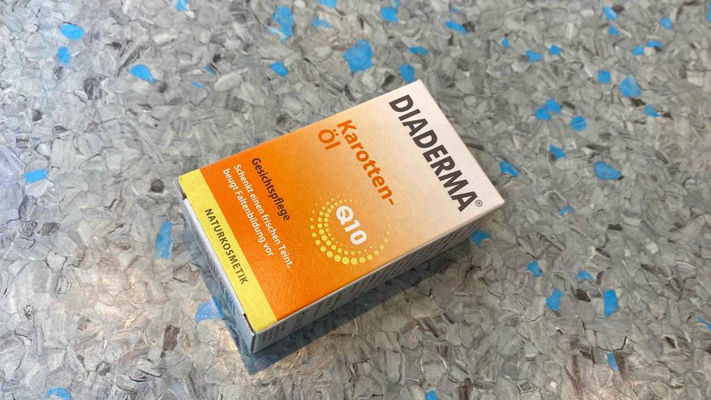 Eine Packung getestetes Karottenöl liegt quer auf einer blaugrauen Fläche.