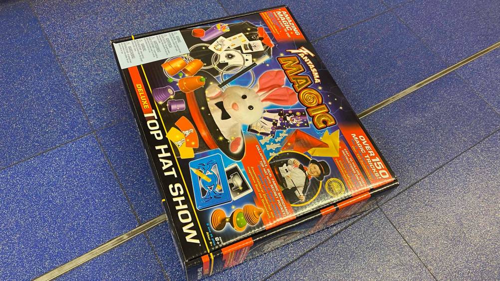 Auf einem blauen Boden liegt ein getesteter Zauberkasten in Originalverpackung.