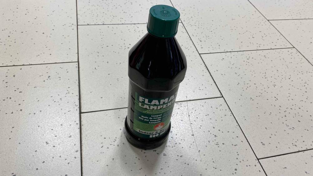 Lampenöl-Test: eine Flasche Lampenöl mit grünem Etikett und Deckel stehend auf einem Boden.
