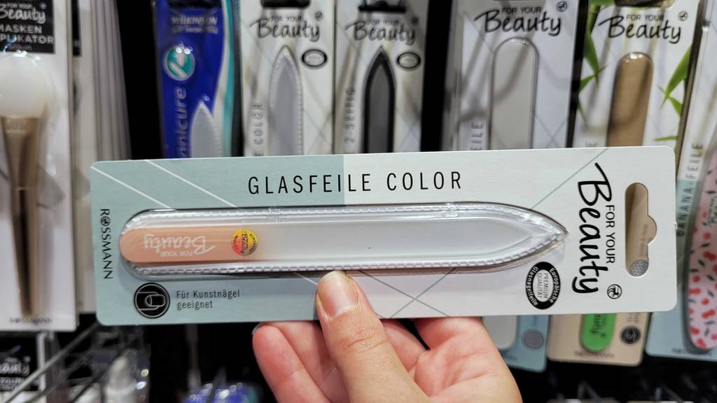 Glasnagelfeile getestet: Eine Hand hält eine verpackte Glasnagelfeile vor ein Regal.