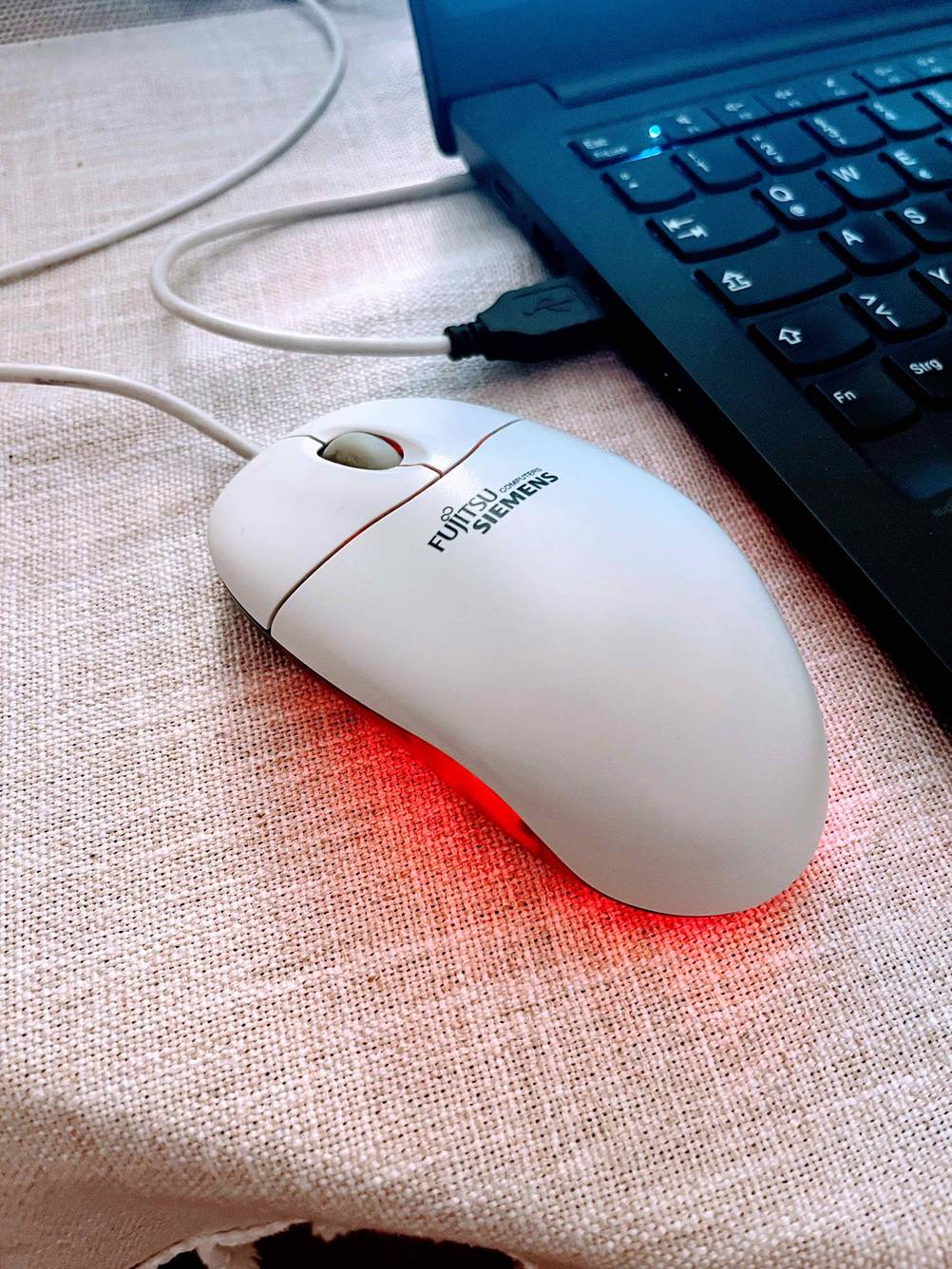 Eine getestete PC-Maus neben einem Computer von schräg oben, die Unterseite leuchtet rot.