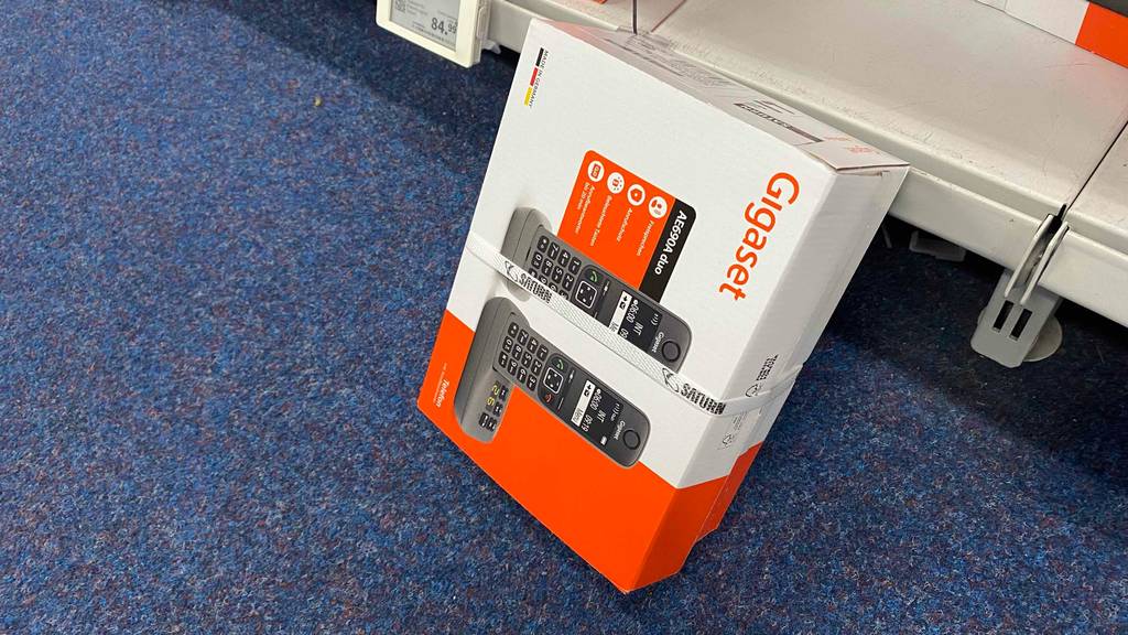 Ein schnurloses Telefon-Duo in Verpackung lehnt an einem Regalbrett.