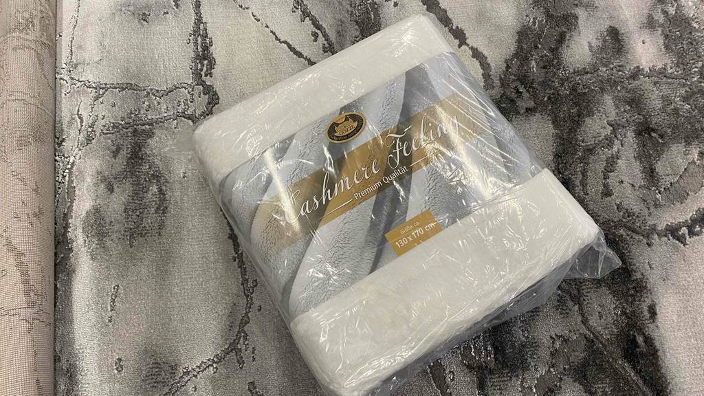 Kaschmirdecke im Test: Die Decke namens Cashmere Feeling liegt in der Originalverpackung auf einem grauen Untergrund.