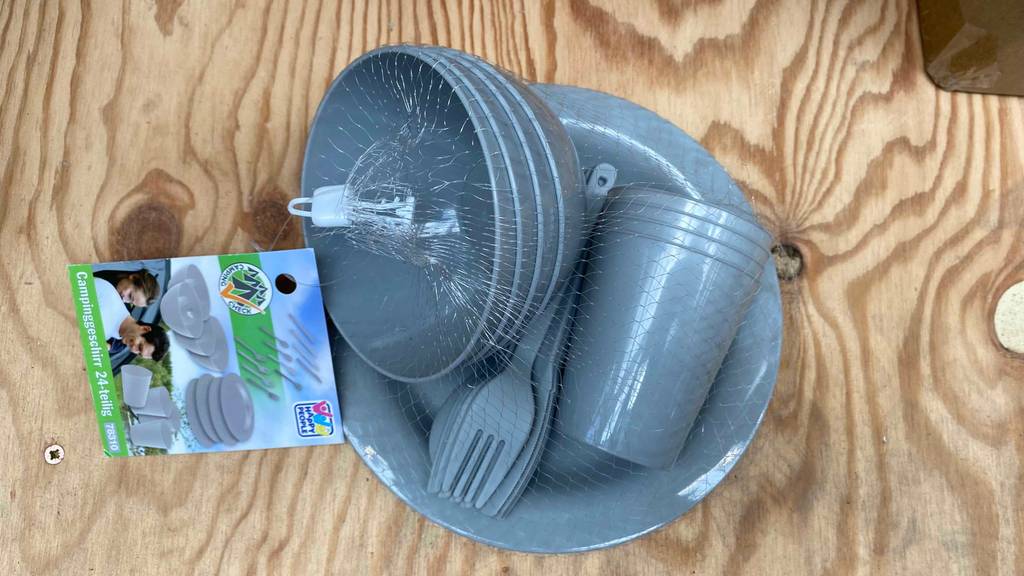 Campinggeschirr im Test: graues Campinggeschirr in einem Netz bestehend aus Schüsseln, Besteck, Becher und Teller.