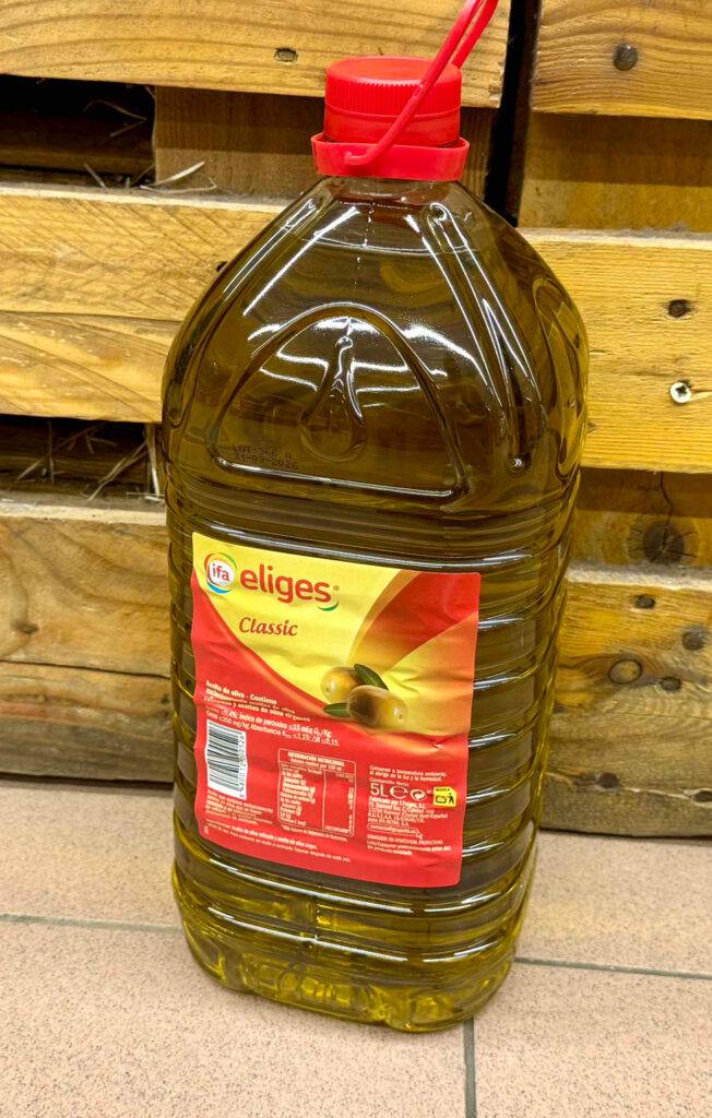 Das getestete Olivenoel im 5-l-Behälter aus transparentem Kunststoff steht vor einer Holzkiste.