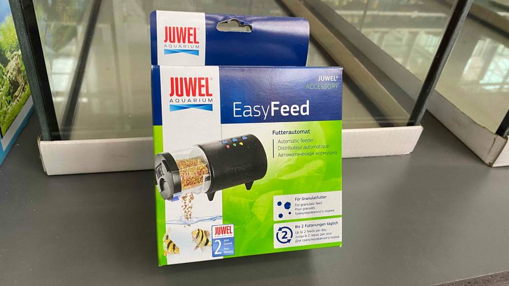 Futterautomat-Aquarium im Test: Verpackung von Futterautomat für Granulatfutter ist an einem Aquarium angelehnt.