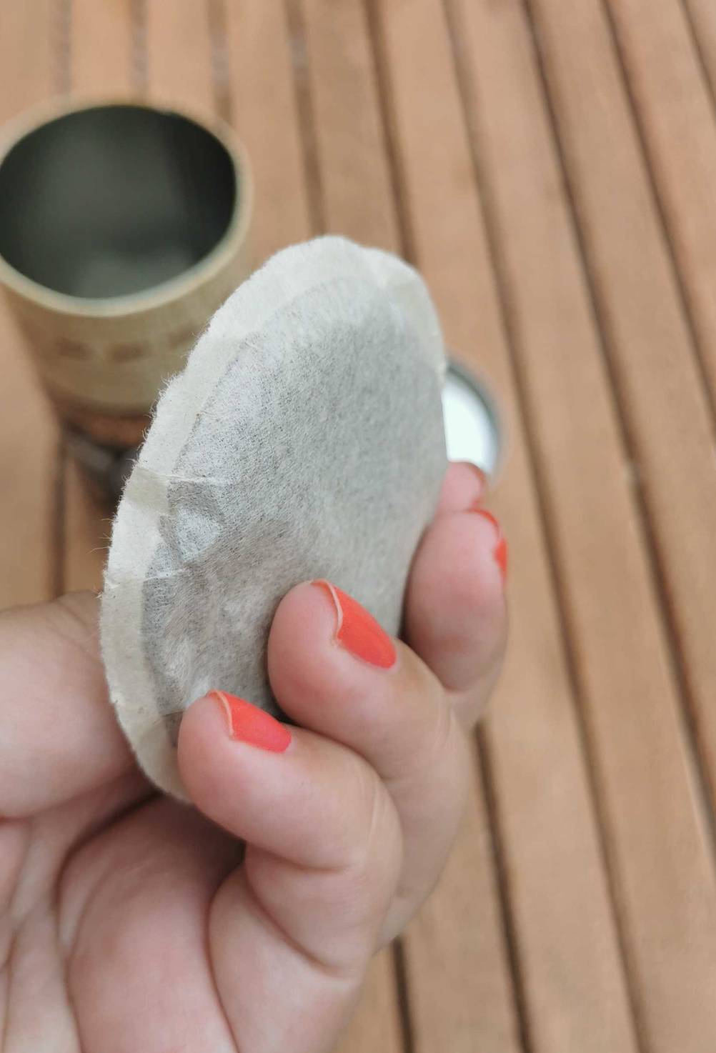 Ein Kaffeepad in der Hand und Dose auf einem Tisch.