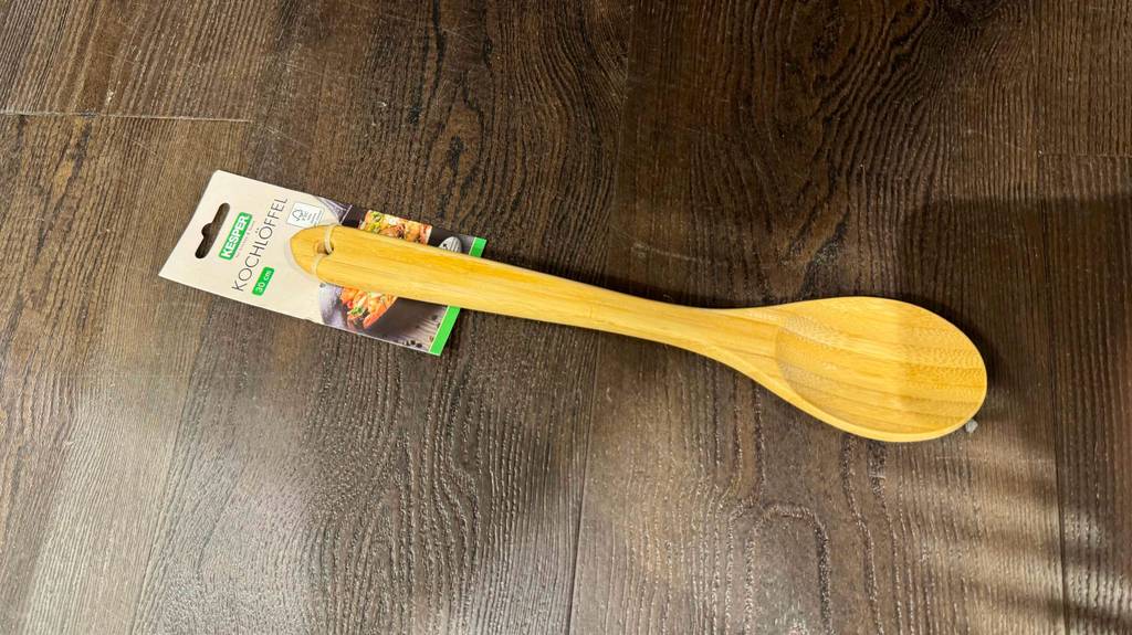 Der getestete Holz-Kochlöffel liegt auf einem dunklen Holzboden.