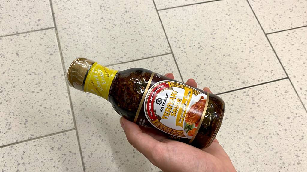 Teriyaki-Sauce getestet: Eine Hand hält eine Flasche Sauce über einen Fließenboden