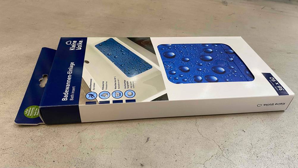 Badewannenmatte im Test: Eine Originalverpackung horizontal auf einem Steinboden