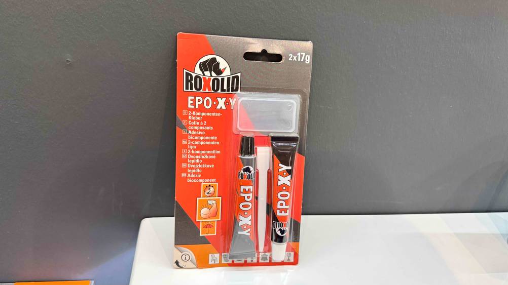 Ein Packung des getesteten 2-Komponenten-Klebers lehnt an einer grauen Wand.