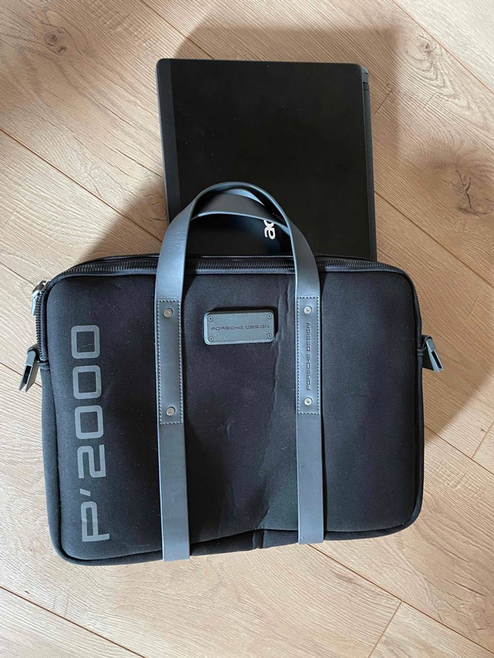 Eine getestete Laptoptasche liegt auf einem Laptop auf einem Holzboden.