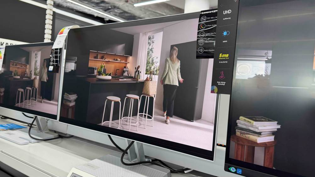 Der getestete Lenovo-Monitor (27 Zoll) steht in einem Regal, während verschiedene Infos zum Modell auf einem Etikett ersichtlich sind.