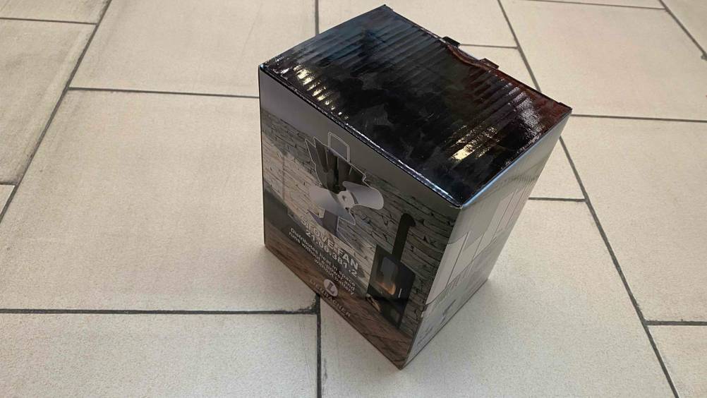 Ofenventilator getestet: Ein verpackter Ofenventilator von schräg oben auf einem Fließenboden.