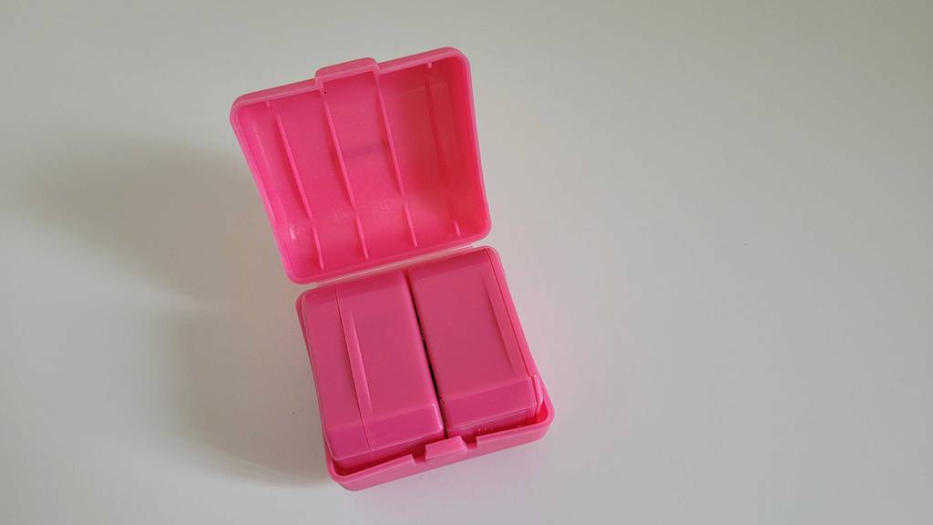 Steckdosenadapter im Test: ein pinkfarbenes Aufbewahrungsbehältnis mit Steckdosenadapter darin, auf einer weißen Fläche liegend.