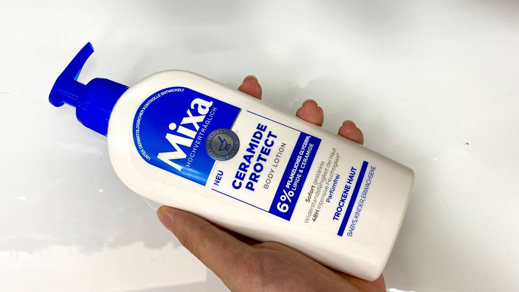 Mixa Bodylotion getestet: Eine Hand hält eine Flasche Lotion vor einen hellen Hintergrund