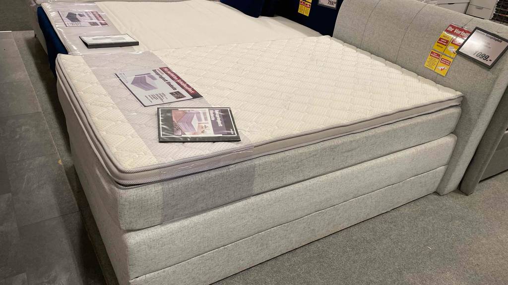 Boxspringbett-120x200 im Test: ein Boxspringbett in Grau in einem Geschäft ausgestellt. 