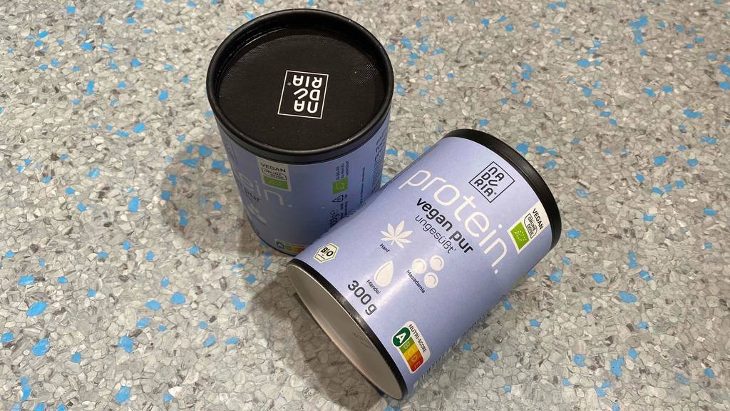 Bio Proteinpulver im Test: Zwei Dosen Pulver, eine liegend, eine stehend auf einem Fliesenboden