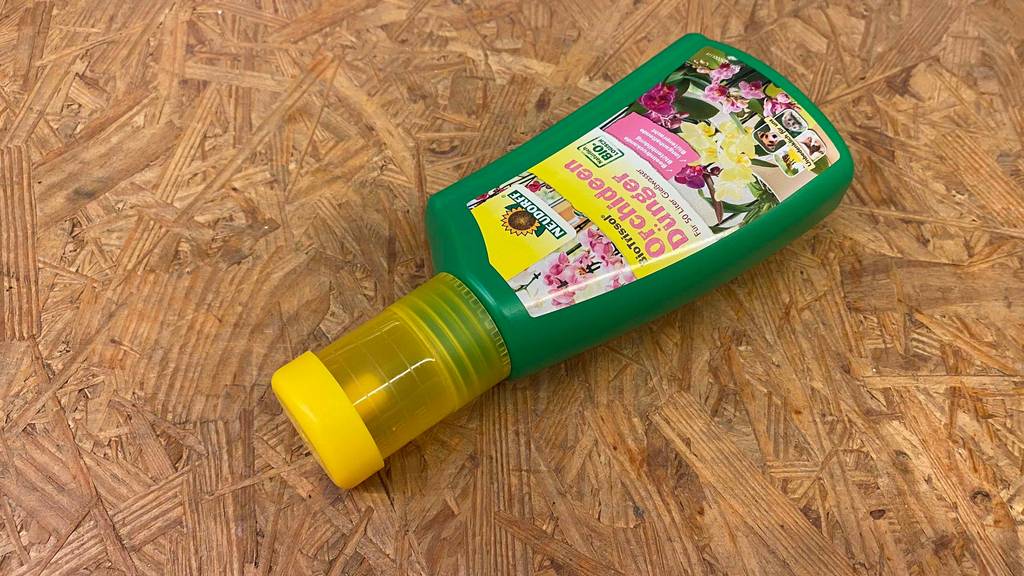 Orchideendünger im Test: Eine Flasche Dünger liegt quer auf einer Holzfläche