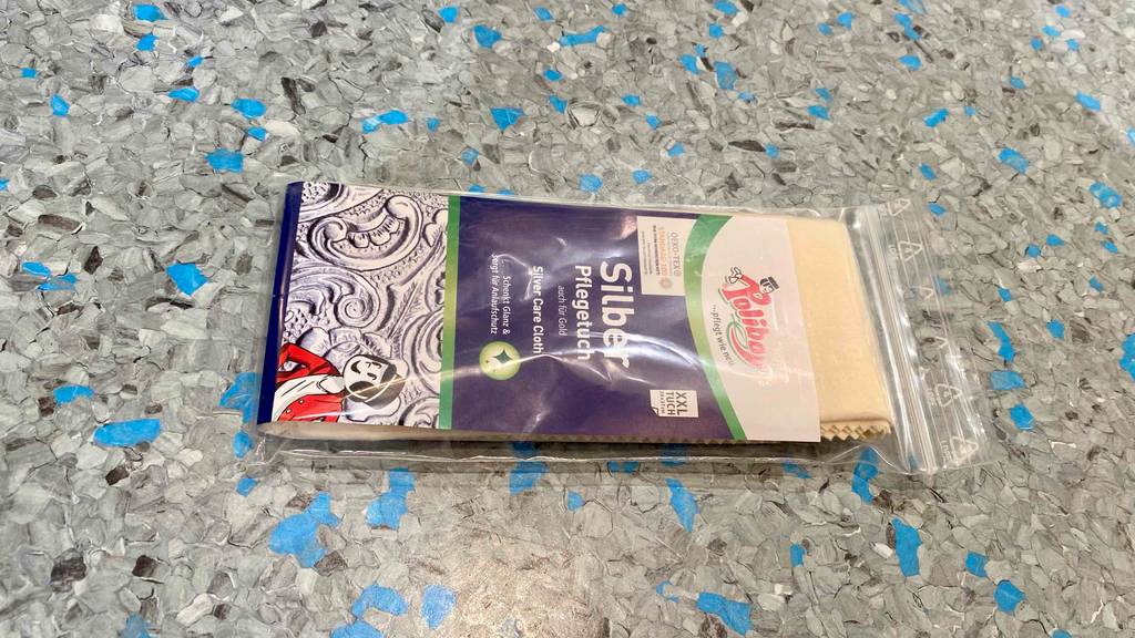 Ein getestetes Silberputztuch in seiner Verpackung horizontal auf einem grauen Boden.