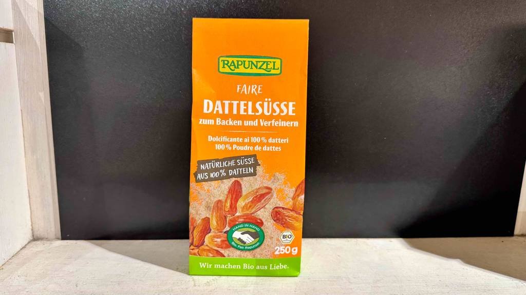 Der Dattelzucker im Test befindet sich in einer orangefarbenen 250-g-Verpackung vor einem schwarzen Hintergrund.