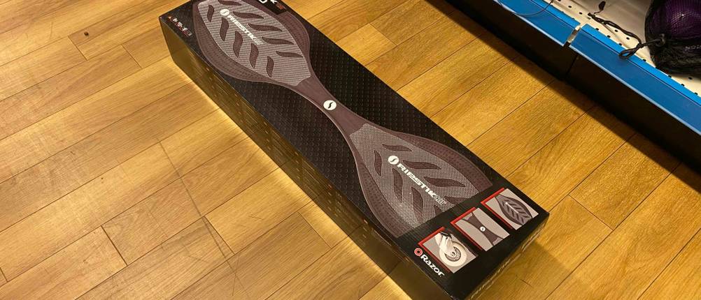 Ein getestetes Waveboard liegt quer auf einem Holzboden vor einem Regal.