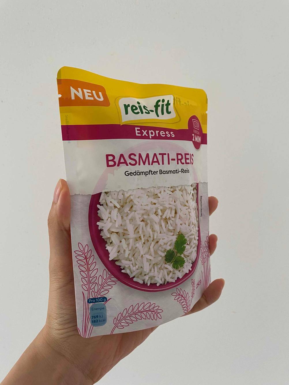 Eine Hand hält eine Packung getesteten Basmatireis vor eine helle Wand.