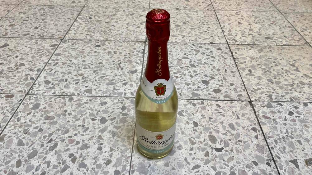 Auf einem Fließenboden steht eine getestete Flasche alkoholfreier Sekt
