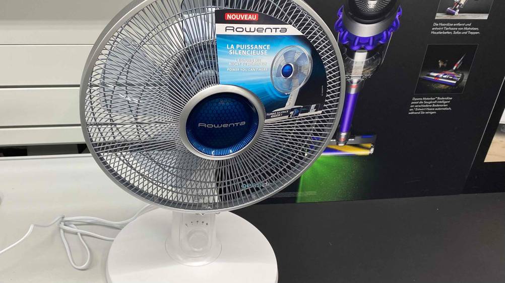 In einer Austellung auf einer dunklen Fläche steht ein getesteter Tischventilator mit Fernbedienung.