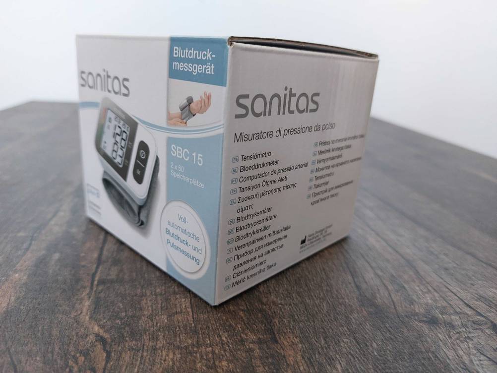 Ein getestetes Sanitas-Blutdruckmessgerät in Originalverpackung auf einer Holzfläche.