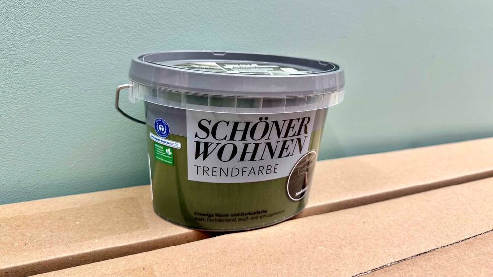 Die getestete grüne Wandfarbe steht vor einer grauen Wand.