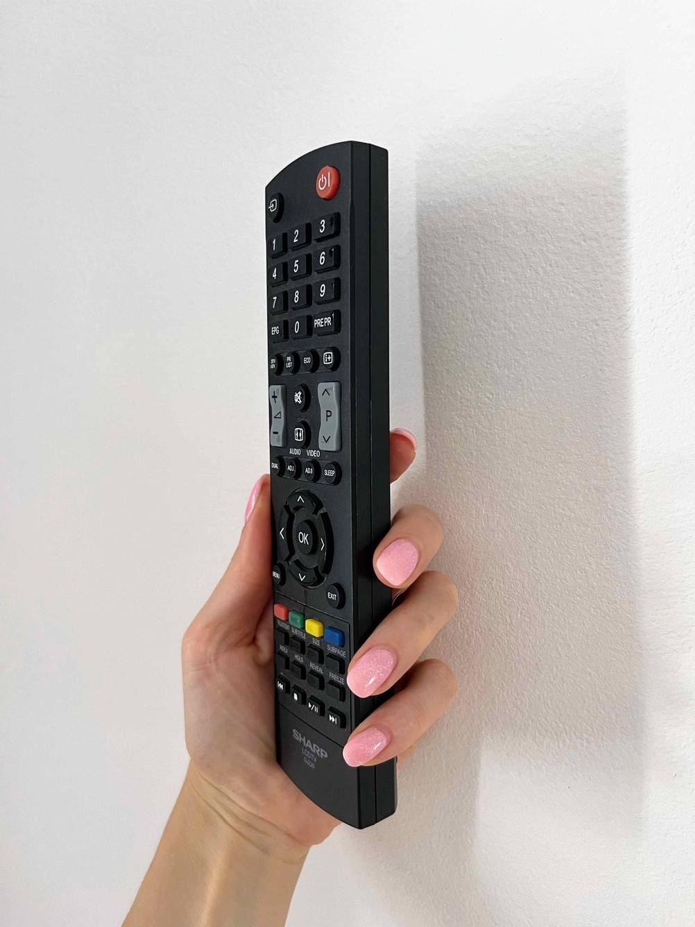 Eine Hand hält eine Universalfernbedienung seitlich vor eine helle Wand.