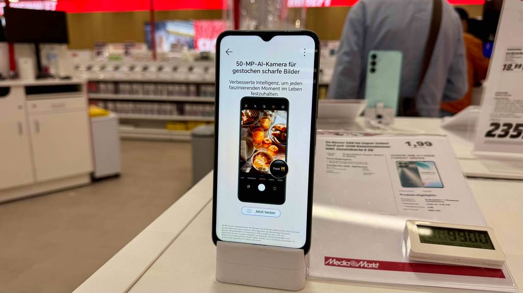 Im Test: Das Smartphone unter 100 Euro steht mit eingeschaltetem Display in einem Media Markt auf dem Ausstellungstisch.
