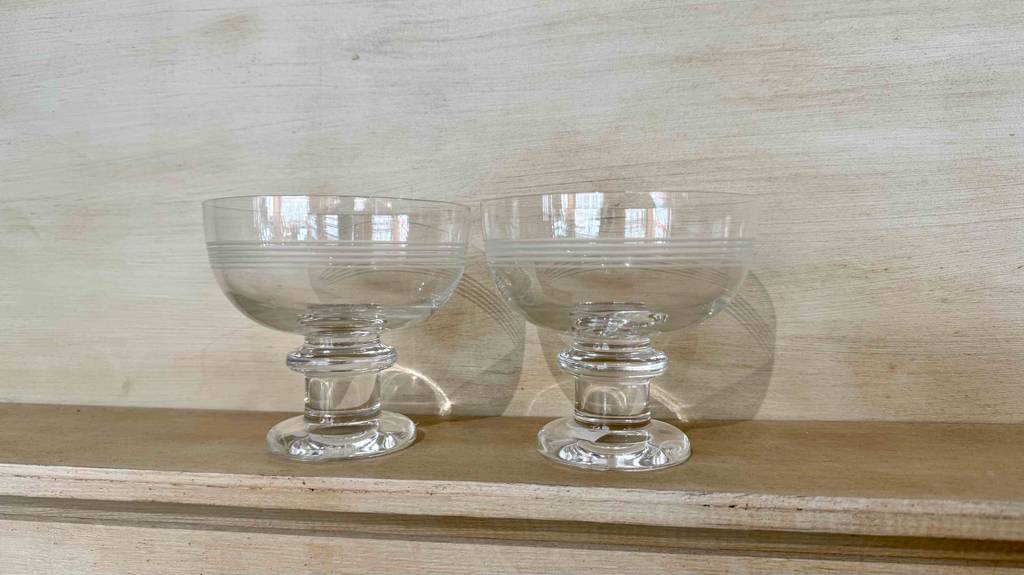Zwei getestete Eisbecher aus Glas stehen vor einer hellgrauen Wand.
