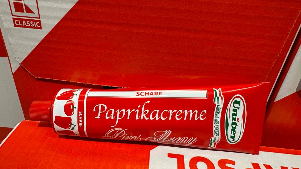 Eine getestete Tube Paprikapaste in Nahaufnahme ist vor Kartons platziert.